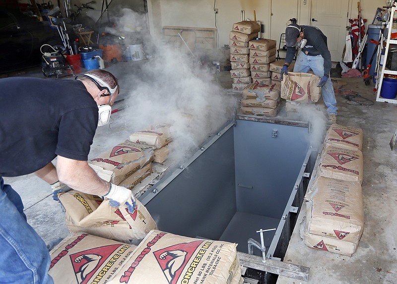 In this Thursday, May 1, 2014 file photo, Jim Hohnsbehn, left, and Jacob Ortiz, of Thunderground Storm Shelters, pour bags of concrete around the sides of a storm shelter during an installation into the garage of a residence in Oklahoma City. Sales of safe rooms are on the rise since a series of devastating twisters hit the Midwest and South in recent years. Forget toasters, blenders and slow cookers. Some engaged couples in Tornado Alley have a more practical gift request: Donations toward safe rooms. 
