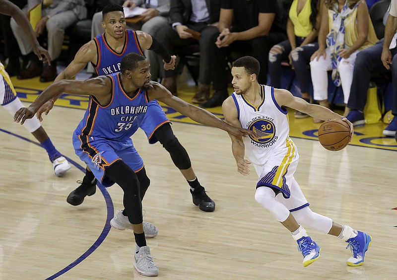 Golden State Warriors guard Stephen Curry dribbles against Oklahoma City Thunder forward Kevin Durant and guard Russell Westbrook, back, during the first half of Game 7 of the Western Conference finals Monday in Oakland, Calif.