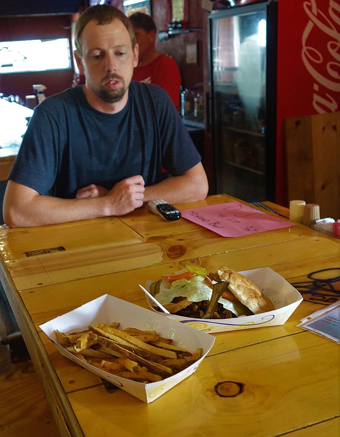 Eric Byrnes, the owner of Mokane Bar and Grill, shows off the Mokane special, a cheesburger topped with pulled pork and onion rings.