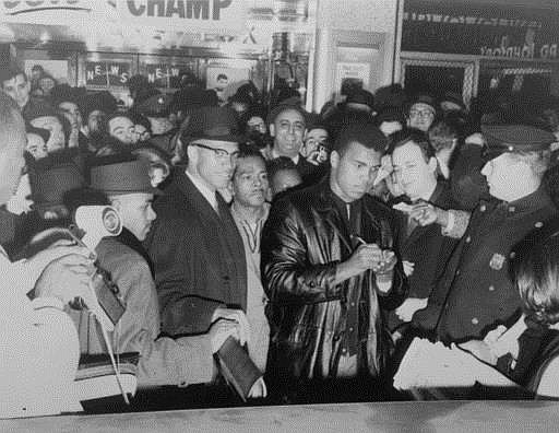 In this March 1, 1964, file photo, world heavyweight boxing champion Cassius Clay (Muhammad Ali) signs autographs outside the Trans-Lux Theater on Broadway at 49th Street in New York City. Standing behind Ali is Malcolm X. Ali, the magnificent heavyweight champion whose fast fists and irrepressible personality transcended sports and captivated the world, died Friday, June 3, 2016. He was 74.