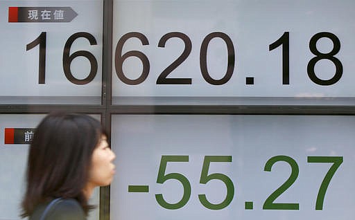 A woman walks past an electronic stock board showing Japan's Nikkei 225 index at a securities firm in Tokyo Wednesday, June 8, 2016. Asian stocks were mostly lower Wednesday after the World Bank cut its global growth forecast and investors looked ahead to Chinese trade data.
