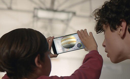 This image provided by Google shows people looking at a view of the solar system using technology Google calls "Project Tango." Tango uses software and sensors to track motions and size up the contours of rooms, which can empower a smartphone to map building interiors. That's a crucial building block of a promising new frontier in "augmented reality," or the digital projection of lifelike images and data into a real-life environment. (Courtesy of Google via AP)