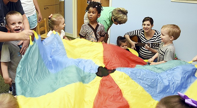As Kristin Veteto, seated on the floor, plays guitar and sings as students raise and lower a parachute to her directions. Veteto spent part of her morning using music to reach the children and observed behavior Monday at the Special Learning Center.