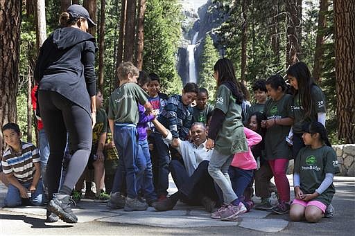 President Barack Obama jokes that he needs help getting up and is assisted by children as he and first lady Michelle Obama met with children during the "Every Kid in a Park" event at Yosemite National Park, Calif., on Saturday, June 18, 2016. The Obama family traveled to Yosemite to celebrate the 100th anniversary of the creation of America's national park system.