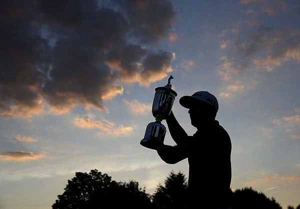 As darkness falls Sunday, Dustin Johnson holds the trophy after winning the U.S. Open at Oakmont Country Club in Oakmont, Pa.