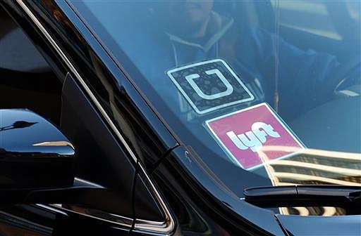 In this Tuesday, Jan. 12, 2016, file photo, a driver displaying Lyft and Uber stickers on his front windshield drops off a customer in downtown Los Angeles. 