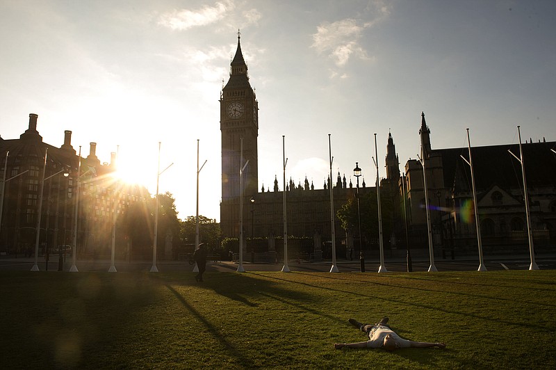 A man lays down on the green in Parliament Square as the sun rises Friday, June 24, 2016, behind the Houses of Parliament in London. Britain voted to leave the European Union after a bitterly divisive referendum campaign, according to tallies of official results Friday.