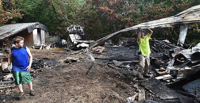 Noah Jinson, 8, left, stears clear as his dad, Scott, tosses a piece of scorched metal siding onto a pile while cleaning up after last week's fire at Don Jinson's shed/workshop on Big Horn Drive.