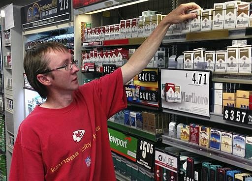 In this June 23, 2016 photo, Charlie Hake, owner of We B Smokin in Jefferson City, Mo., reaches for a pack of cigarettes at his store. Hake opposes a pair of proposed Missouri ballot initiatives seeking to raise the state's lowest-in-the-nation cigarette tax. 