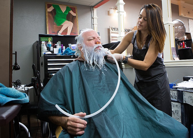 Mark Reed breathes through a hose Friday as Jessica Gray bleaches his beard, eyebrows and hair at Shear Country Salon in Texarkana, Texas. Reed is getting ready for the Discover Santa 2016 convention in Branson, Mo. 
