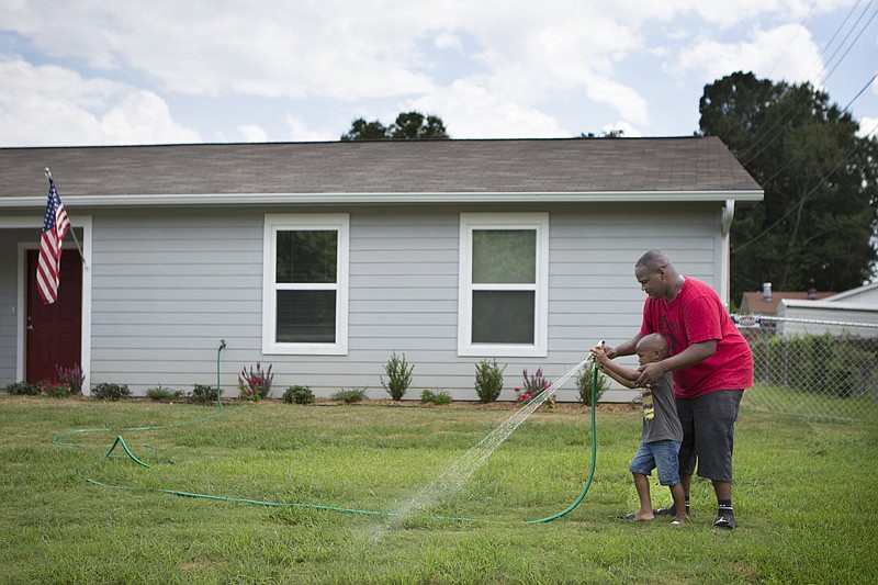 Darrell Burks waters the lawn of his sister Kinisha Burks on Monday with help from his son, Kev. Kinisha Burks recently moved into the house on Norris Cooley Drive that was built by Habitat for Humanity. Temperatures are expected to reach triple digits this week.