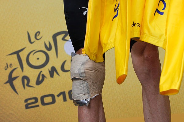 With his knee bandaged after a crash, Chris Froome prepares to put on the overall leader's yellow jersey on the podium after Friday's stage of the Tour de France in Saint-Gervais Mont Blanc, France.
