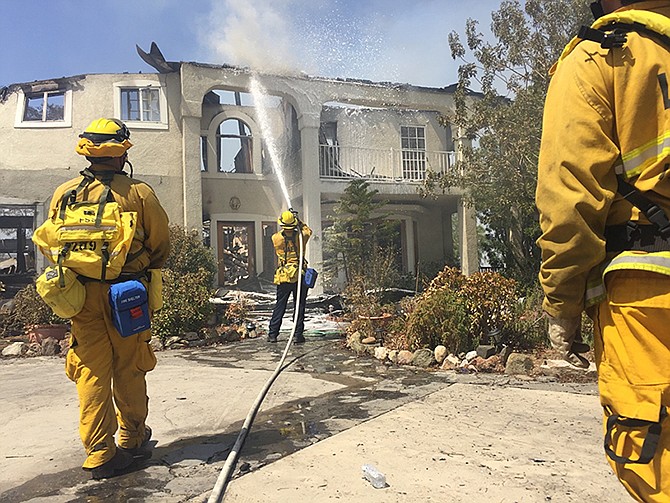 Firefighters use foam to put out flare ups on a home Sunday at the end of Iron Canyon in Santa Clarita, California. Authorities say 18 homes have been destroyed and an additional 1,500 are threatened as crews battle a massive wildfire in wooded canyons north of Los Angeles. The blaze has blackened more than 34 square miles of dry brush withered by days of triple-digit heat on the edge of the Angeles National Forest. It was just 10 percent contained Sunday.