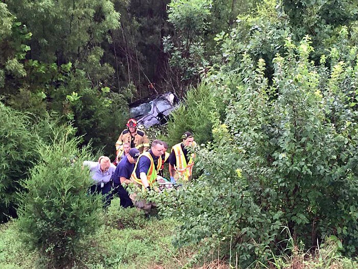 Firefighters and EMTs carry Margert Savage up a steep embankment after her vehicle plunged down the hillside near Route B and U.S. 54.