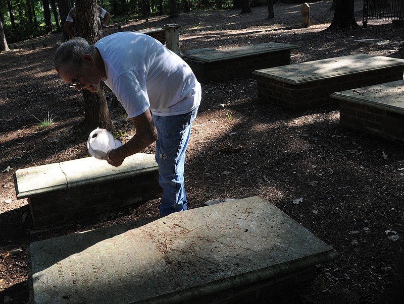  Eugene Stanton brushes away leaves so that he can read bunker-type gravestones for Charles and Mary Harrison Moores in the old Harrison Chapel Cemetery.
