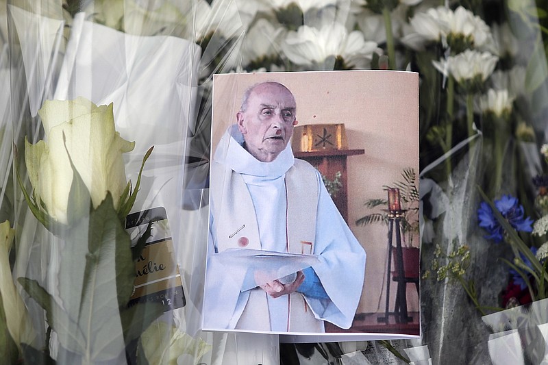 A picture of late Father Jacques Hamel is placed on flowers Wednesday, July 27, 2016, at the makeshift memorial in front of the city hall near the church where an hostage taking left a priest dead the day before in Saint-Etienne-du-Rouvray, Normandy, France. The Islamic State group crossed a new threshold Tuesday in its war against the West, as two of its followers targeted a church in Normandy, slitting the throat of an elderly priest celebrating Mass and using hostages as human shields before being shot by police.