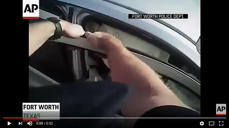 This screen capture taken from body cam video shows a Fort Worth, Texas, police officer trying to free a robbery suspect from a burning vehicle after a chase that ended with a crash.