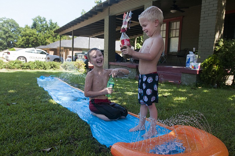 Brothers Trey Mays, left, and Owen Cooper enjoy a slip-n-slide Monday in their front yard on East 15th Street.