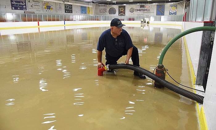 Above, Jefferson City firefighter Buck Protzman holds down an intake hose in the shallow water on the ice arena floor. He was part of one crew trying to get the floodwater off of the arena floor. 