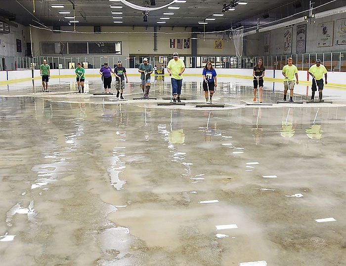 Pushing squeegees and rollers, volunteers and Parks and Recreation employees remove water from the concrete surface of the ice rink in Washington Park. 