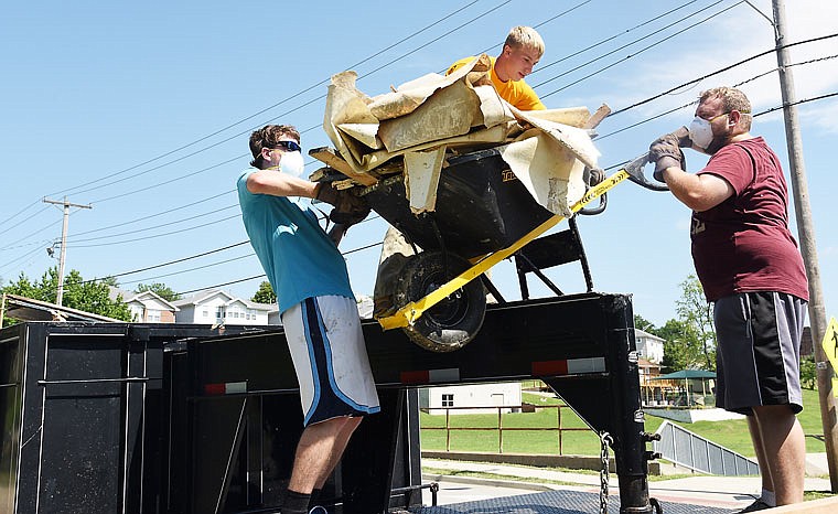 Volunteers from Adolos Ministry in Springfield, Tim Stone, left, and Collin Sansom, right, assist Aaron Sturgeon, a volunteer from the Missouri Baptist Convention Disaster Relief Collegiate Team, hoist a wheelbarrow full of debris to a trailer full of wet drywall, furniture, carpet pieces and other items from the basement of the East Side Community Center, which was damaged in this week's flash flooding.