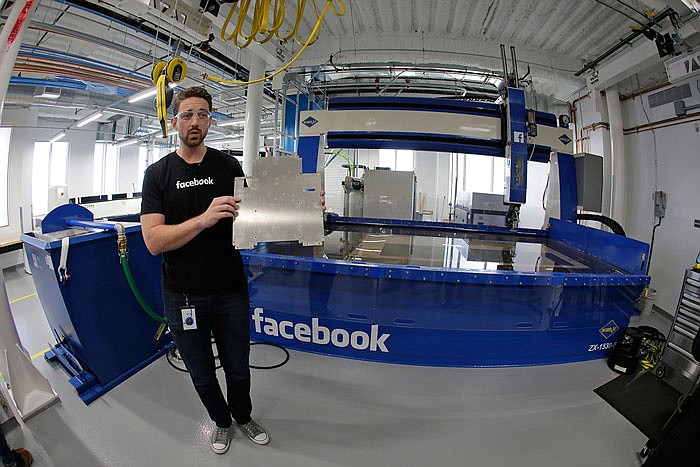 Model maker Spencer Burns, holds up a piece of sheet metal while standing in front of a water jet during a tour of Area 404, the hardware R&D lab, at Facebook headquarters in Menlo Park, Calif.