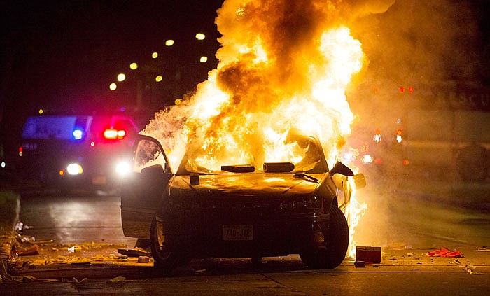 A car burns as a crowd of more than 100 people gathers following the shooting of a man in Milwaukee.