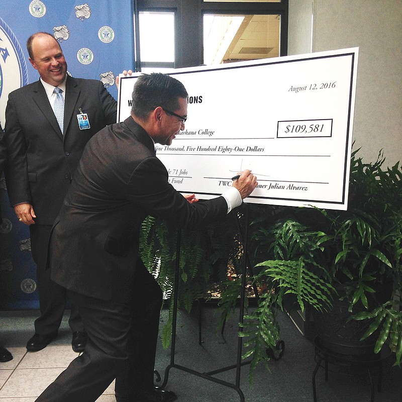 Julian Alvarez, commissioner with the Texas Workforce Commission, signs a $109,581 check to Texarkana College for a Skills Development Fund grant to fund technical training at Alcoa's plant in Nash, Texas. Alvarez said the plant's reopening will have a $6.3 million impact on the area.
