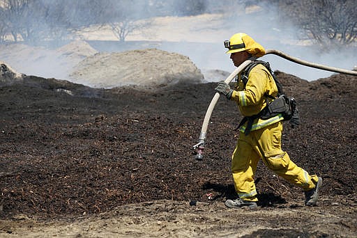 Firefighters water down scorched compost material at a property burned near Phelan, Calif., on Friday, Aug. 19, 2016. The wildfire unleashed its initial fury on a semi-rural landscape dotted with small ranches and homes in Cajon Pass and on the edge of the Mojave Desert before climbing the mountains.