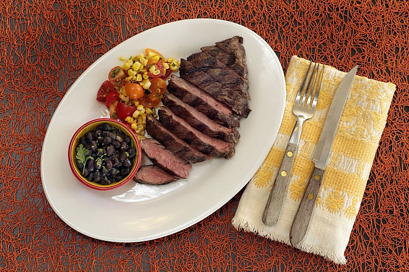 This Aug. 4, 2016 photo shows skirt steak with beer-braised black beans and corn salsa, styled by Sarah Abrams, displayed at the Institute of Culinary Education in New York. This dish is from a recipe by Elizabeth Karmel.