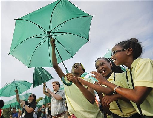 Randle Highlands Elementary School fourth graders, center, from left, Zaria Russell, Zani La McElwain, and Kelsi Williams raise their umbrella while assembling into a living version of the National Park Service's iconic Arrowhead emblem, near the Washington Monument on the National Mall in Washington, Thursday, Aug. 25, 2016. More than 1,000 participants used brown, green and white umbrellas to create the emblem during an event that took place on the 100th anniversary of the creation of the National Park Service. They also posed for a group photo that was being taken from a helicopter hovering overhead.