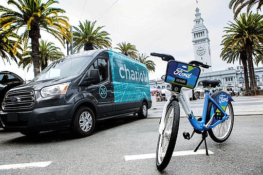 This Thursday, Sept. 8, 2016, photo taken in San Francisco and provided by Ford Motor Company shows a Ford Transit passenger van operated by Chariot shuttle service and a bicycle operated by bike-share company Motivate. Ford Motor Co. announced Friday, Sept. 9, 2016, it is buying the app-based shuttle service Chariot and is partnering with bike-share company Motivate as part of its ongoing effort to expand its traditional business. 