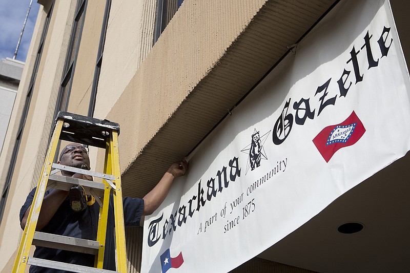 Steve Williams, maintenance supervisor with the Texarkana Gazette, installs a temporary sign Monday at the entrance of the Gazette's new office in the Landmark Building at 101 E. Broad St.
