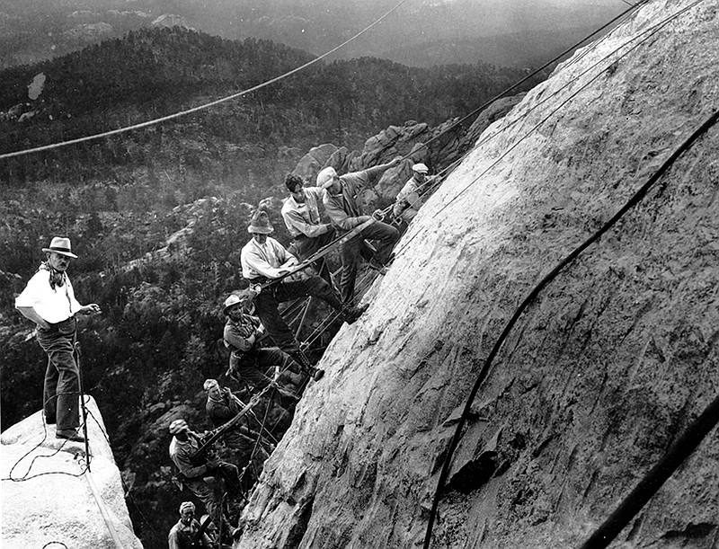 Sculptor Gutzon Borglum, at left, directs drillers suspended by cables from the top of the mountain as they work on the head of President George Washington in 1929 at the Mount Rushmore Memorial.