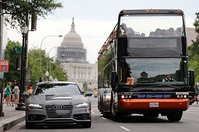 A double decker tour bus drives by an Audi self-driving vehicle parked on Pennsylvania Avenue, near the Capitol in Washington, D.C.

