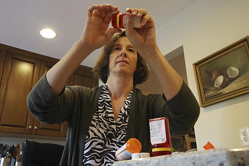 In this Sunday, Sept. 18, 2016, photo, Shelley Ewalt sits in her home, in Princeton, N.J., near an open amber-colored CVS pharmacy prescription bottle, as she opens one of two uniquely designed red ones from Target. After CVS took over operation of Target's drugstores earlier this year, distraught customers have been asking the drugstore chain to bring back the retailer's red prescription bottles, which came with color-coded rings, labeling on the top and prescription information that was easier to read. Ewalt tweeted to the drugstore chain, asking if there was any chance they might return to the design of the Target bottles, which she found easier to open.