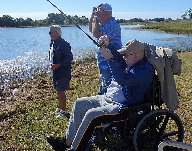 Arlon Fowler, right, reels in a fish Monday at a private lake west of Fulton.