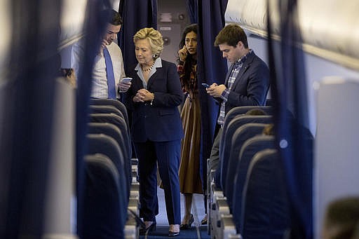 Democratic presidential candidate Hillary Clinton, accompanied by senior aid Huma Abedin, second from right, and traveling press secretary Nick Merrill, right, speaks with national press secretary Brian Fallon, left, aboard her campaign plane in White Plains, N.Y., Monday, Oct. 3, 2016, before traveling to Toledo, Ohio.