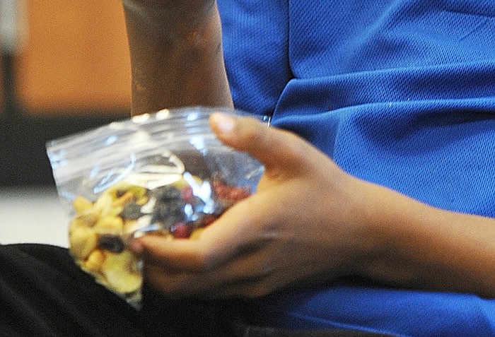 An elementary student samples trail mix. 