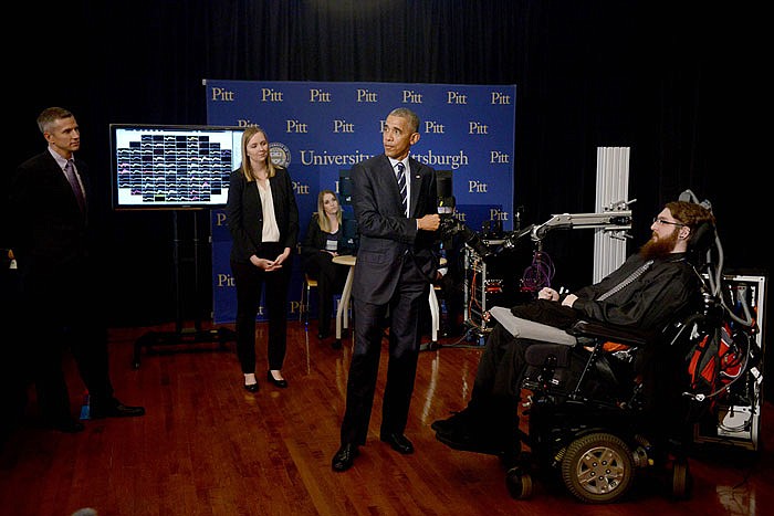 President Barack Obama holds a robotic arm being controlled by the mind of the man in the wheel chair at right as he makes a stop at the exhibition hall of the White House Frontiers Conference.
