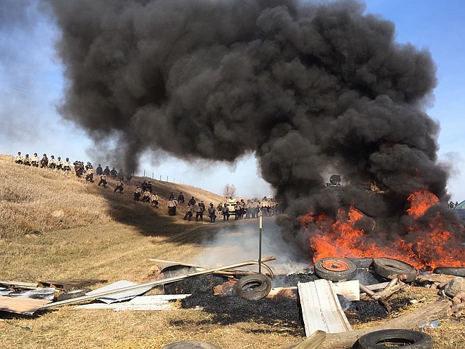 Tires burn as armed soldiers and law enforcement officers stand in formation Thursday to force Dakota Access pipeline protesters off private land where they had camped to block construction. The pipeline is to carry oil from western North Dakota through South Dakota and Iowa to an existing pipeline in Patoka, Illinois.