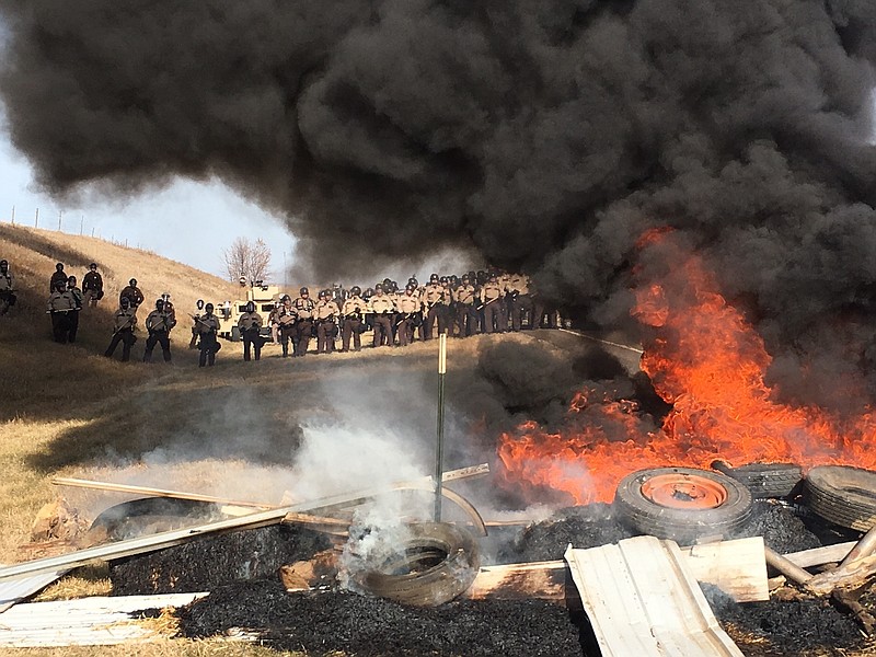 Tires burn as armed soldiers and law enforcement officers stand in formation on Thursday, Oct. 27, 2016, to force Dakota Access pipeline protesters off private land where they had camped to block construction. The pipeline is to carry oil from western North Dakota through South Dakota and Iowa to an existing pipeline in Patoka, Ill. 