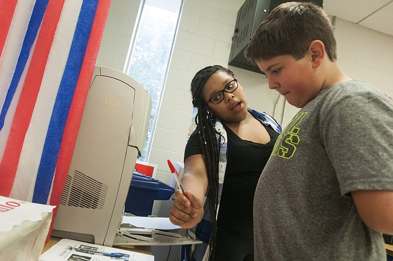 College Hill Elementary student Seth Coker, right, looks down at his presidential ballot as Alysa Greene explains the voting process during a mock election Monday in Melissa Estes' class. The voting booth was a project by Greene.
