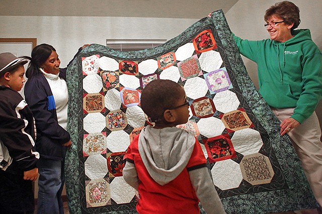 From far left, Gage McCombs 9, Judith McCombs, Prys McCombs, 3, and Colleen Carl unveil a quilt made by the Missouri River Quilt Guild celebrating the construction of a new home Thursday in Jefferson City. The McCombs' home is the 100th house to be built by River City Habitat for Humanity and was completed in less than 100 days.