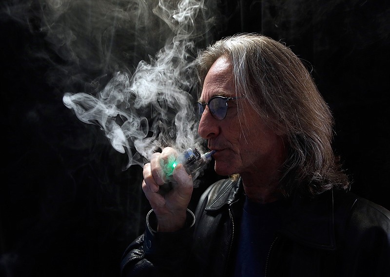 In this Dec. 4, 2013, file photo, John Hartigan, proprietor of Vapeology LA, a store selling electronic cigarettes and related items, takes a puff of an electronic cigarette at his store in Los Angeles. As smoking declines nationwide, states are increasingly turning to taxing electronic cigarettes, a trend that concerns some public health experts who fear it could deter smokers from switching to the safer alternative. California became the seventh state to tax e-cigarettes after voters Nov. 8, 2016, overwhelmingly approved a ballot measure.