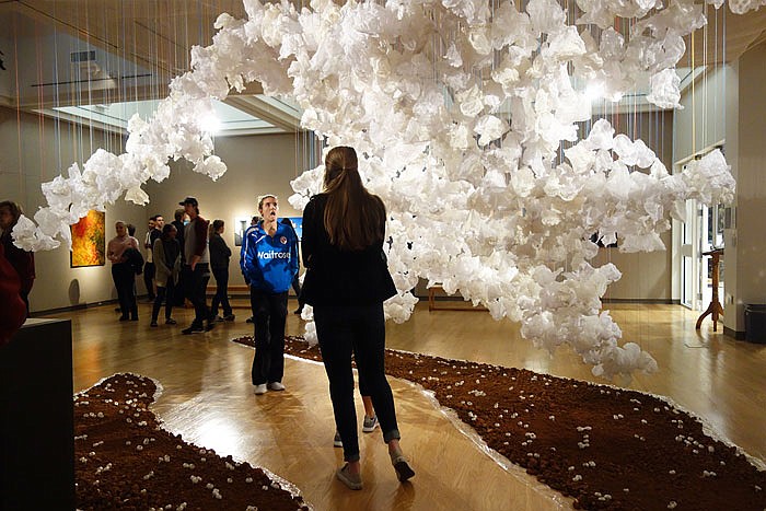 Students interact with art at William Woods University's faculty art show. The installation in the foreground, titled "While We Tread Lightly," is the work of Valerie Wedel and includes dozens of tiny clay pods and soil from her father's farm.