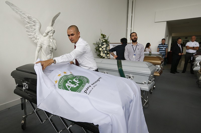 A funeral employee places a white sheet with a Chapecoense soccer team logo over a casket containing the remains of a team member, in Medellin, Colombia, Thursday, Dec. 1, 2016. Forensic authorities say they have managed to identify a majority of the victims of Monday's Colombian air tragedy and hope to finish their work on Thursday.