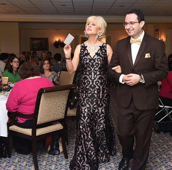 Wearing a full-length evening gown from Saffees, Roni Flood looks to see who is motioning to her as she is escorted by Dr. Shadi Haddadin, an oncologist/hematologist at JCMG, in the third annual Strut Your Style fashion show and luncheon Dec. 5 to benefit the Community Breast Care Project.
