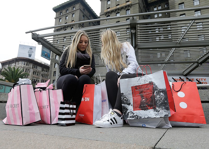 In this Nov. 25, 2016, file photo, Maddy, left, and her friend Maggie, sit with their shopping bags at Union Square in San Francisco. The holiday shopping season is losing some of its power in the year's sales. November and December now account for less than 21 percent of annual retail sales at physical stores, down from a peak of over 25 percent. The shift is in part because people are spreading out their shopping all year, demanding big discounts and spending more on events rather than more stuff. 