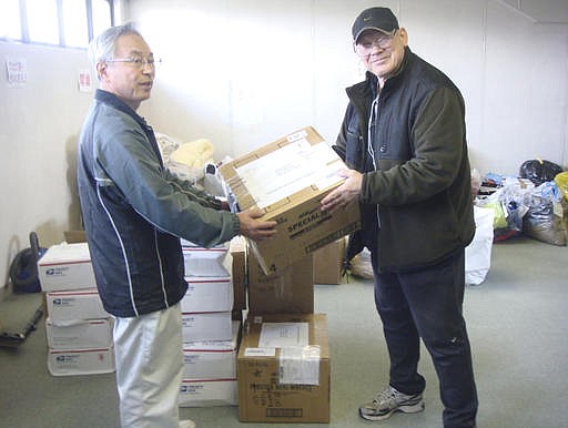 In this photo provided by Joseph Roginski, taken May 13, 2011, Joseph Roginski, right, holds a package in a storeroom of the Misawa City Hall in Japan, where donations of clothing and supplies were being kept for earthquake relief efforts. He says that while the cost of living is higher in Japan, access to health care is not.